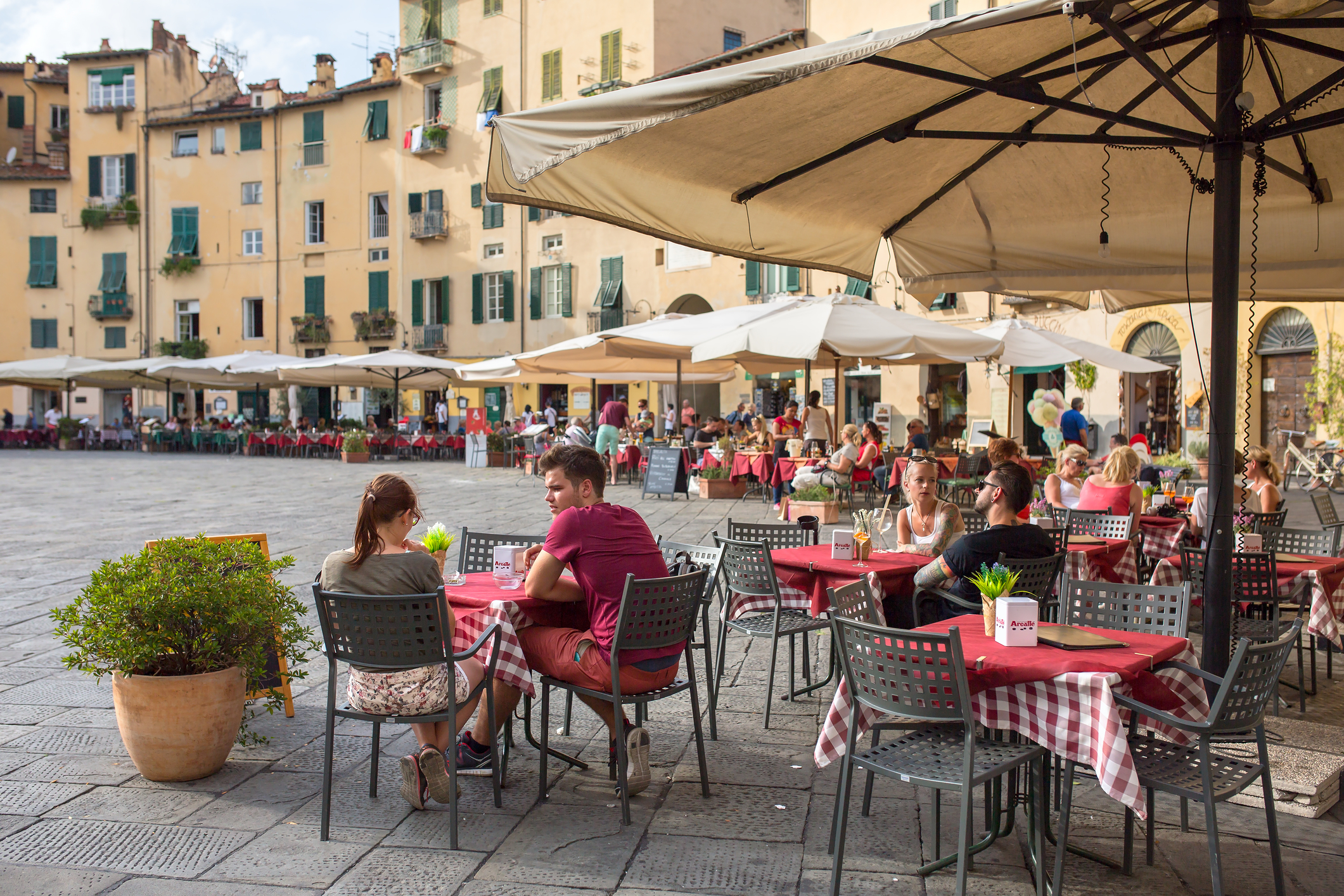 Persoane neidentificate care mănâncă preparate tradiționale italiene într-un restaurant în aer liber în centrul orașului Lucca, Italia. Sursă foto: Dreamstime
